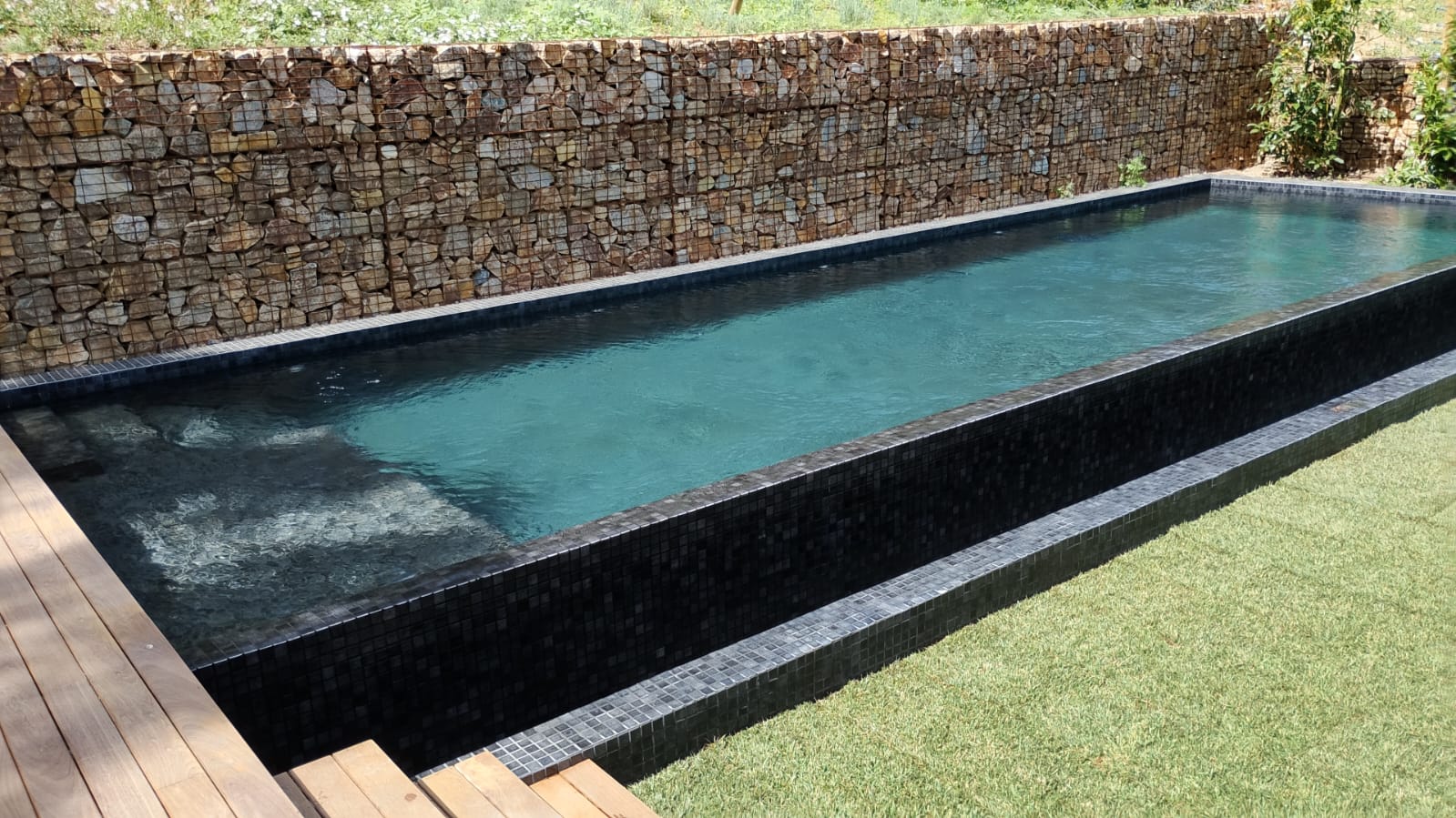 Piscina con revestimiento de mosaico mineral oscuro y muros de gaviones